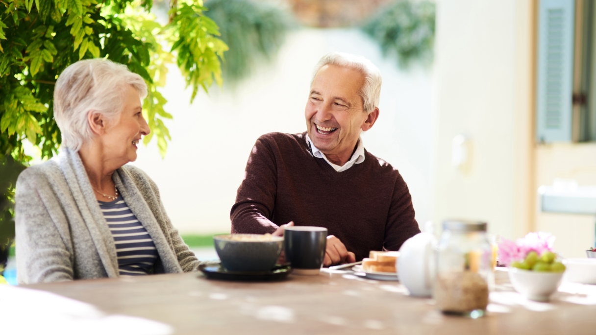 An elderly man and woman laughing sat at a table